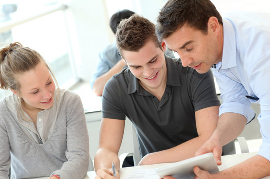 Three students stand around a table and work together.